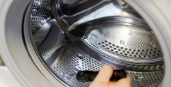 How to remove small items caught behind the drum from a washing machine